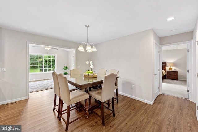 dining space featuring wood-type flooring and ceiling fan with notable chandelier