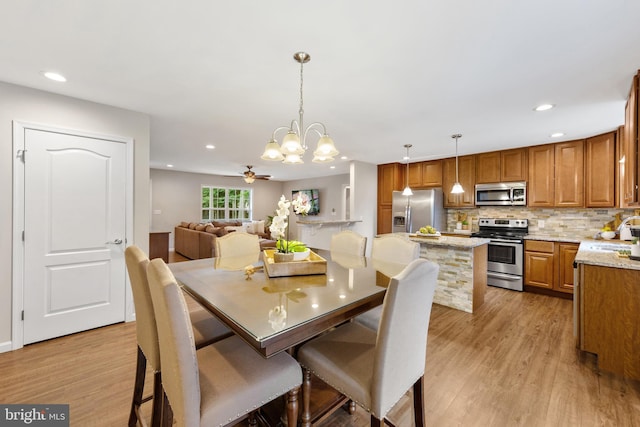 dining area featuring light wood-type flooring, ceiling fan with notable chandelier, and sink