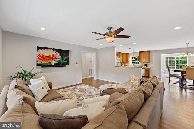 living room featuring ceiling fan with notable chandelier and light hardwood / wood-style flooring