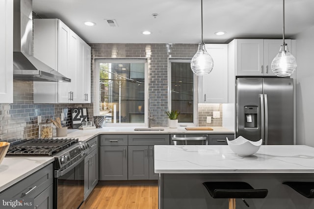 kitchen with light stone counters, gray cabinetry, light hardwood / wood-style flooring, wall chimney range hood, and stainless steel appliances