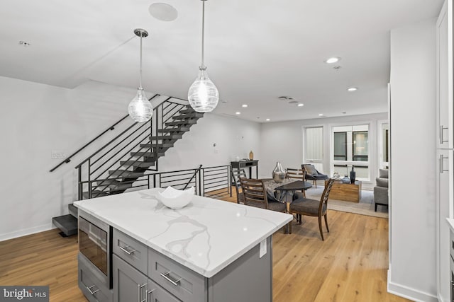 kitchen featuring pendant lighting, gray cabinets, light wood-type flooring, and stainless steel microwave