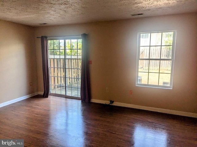 spare room featuring a textured ceiling, dark hardwood / wood-style floors, and plenty of natural light