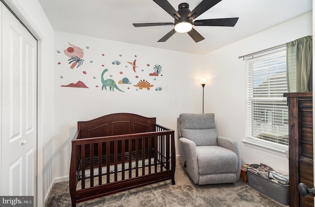 bedroom with a closet, ceiling fan, a crib, and carpet flooring