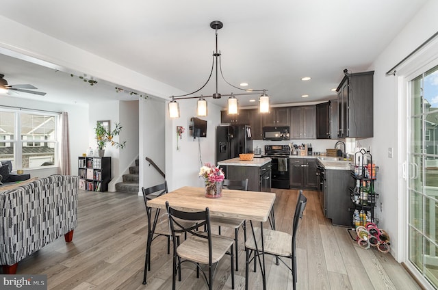 dining space with ceiling fan with notable chandelier, sink, and light hardwood / wood-style flooring