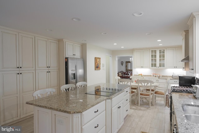 kitchen with appliances with stainless steel finishes, light stone countertops, a breakfast bar area, a center island, and extractor fan