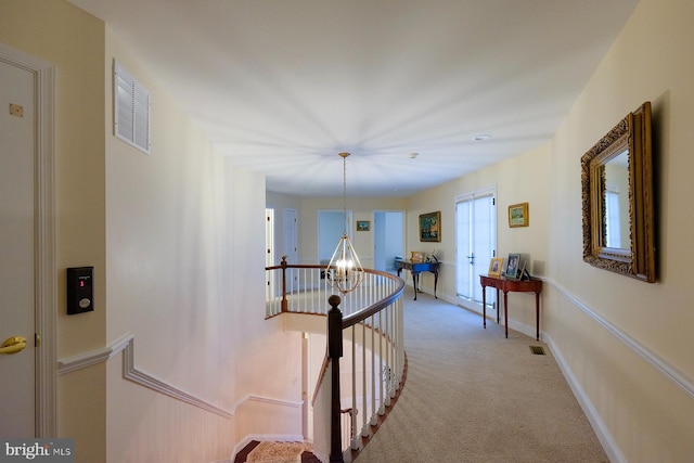 hallway with an inviting chandelier and light colored carpet