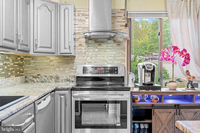 kitchen with gray cabinetry, island range hood, appliances with stainless steel finishes, light stone countertops, and decorative backsplash