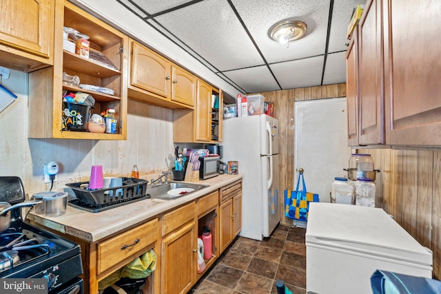 kitchen with white refrigerator, wood walls, a drop ceiling, black range, and sink