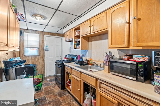 kitchen with black range with gas stovetop, wood walls, sink, and a paneled ceiling