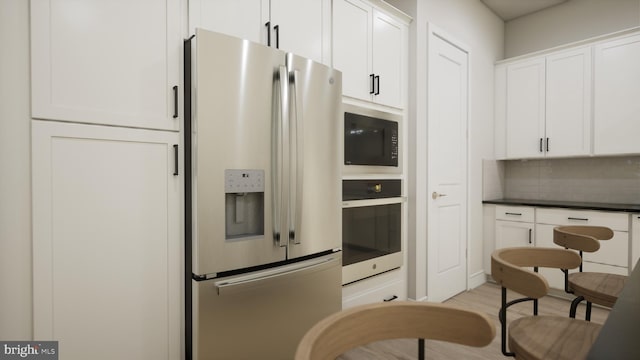 kitchen with light wood-type flooring, stainless steel appliances, white cabinetry, and tasteful backsplash