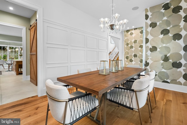 dining room featuring a barn door, light hardwood / wood-style flooring, and a notable chandelier