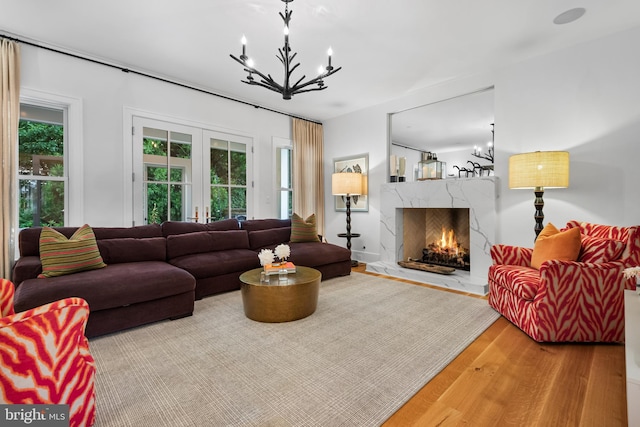 living room with french doors, a notable chandelier, a premium fireplace, and hardwood / wood-style flooring