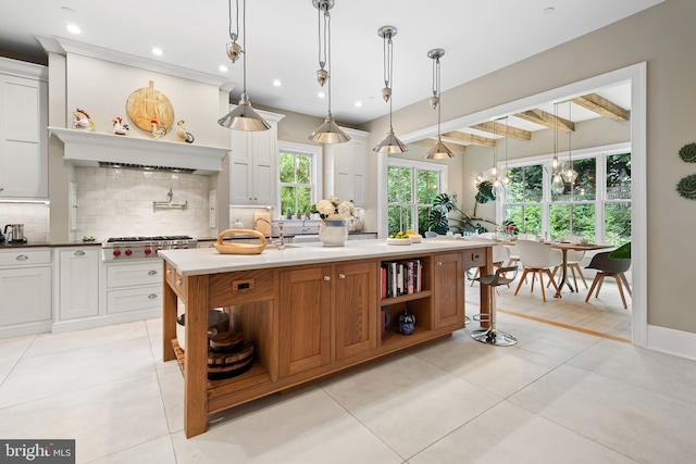 kitchen with hanging light fixtures, beam ceiling, a kitchen island with sink, and white cabinets