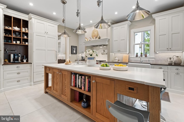 kitchen with decorative backsplash, white cabinetry, hanging light fixtures, and a large island with sink