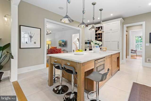 kitchen featuring white cabinetry, a kitchen island, a breakfast bar area, light tile patterned floors, and decorative light fixtures