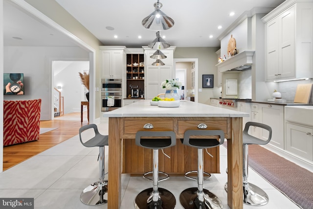 kitchen with a kitchen island, light wood-type flooring, white cabinetry, and decorative light fixtures