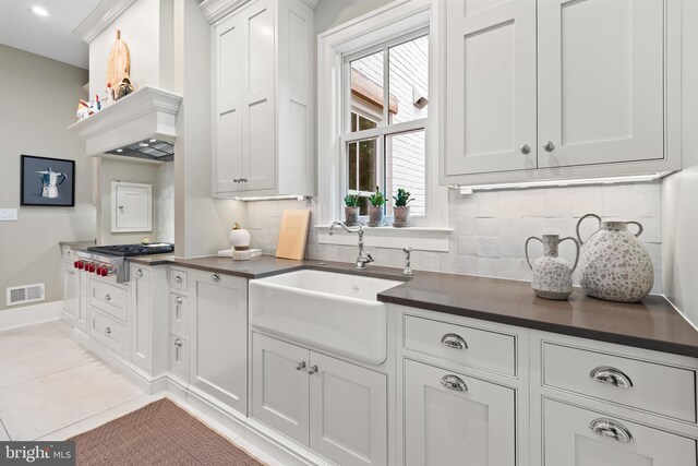 kitchen with light tile patterned flooring, white cabinets, backsplash, stainless steel gas stovetop, and sink