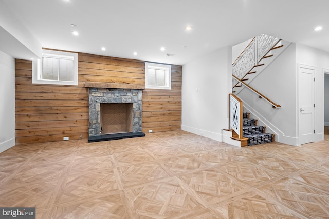 unfurnished living room featuring light parquet flooring, a fireplace, wood walls, and a wealth of natural light