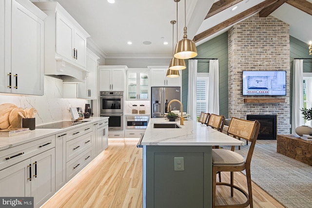 kitchen with light wood-style floors, a sink, a brick fireplace, and appliances with stainless steel finishes