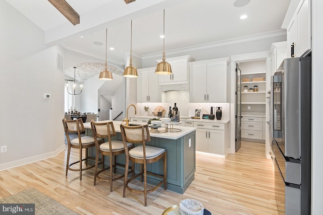 kitchen featuring light countertops, white cabinetry, an island with sink, and freestanding refrigerator