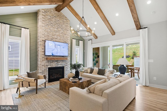 living room with beam ceiling, a brick fireplace, light wood-style flooring, and a chandelier