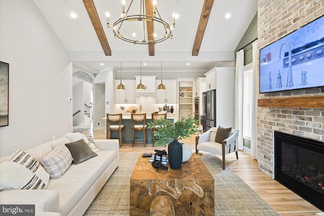 living room with light wood-style floors, a fireplace, stairway, lofted ceiling with beams, and an inviting chandelier