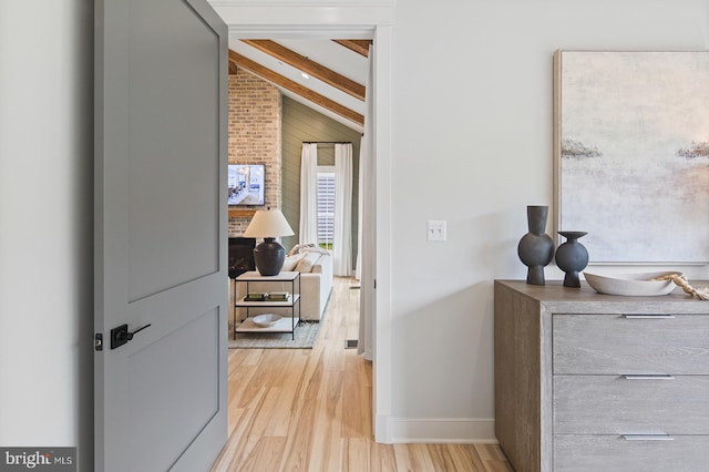 corridor featuring wooden walls, baseboards, light wood-style flooring, and beam ceiling