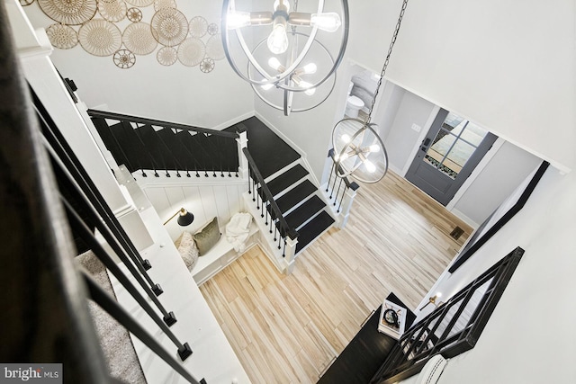 stairway with baseboards, a notable chandelier, wood finished floors, and a towering ceiling