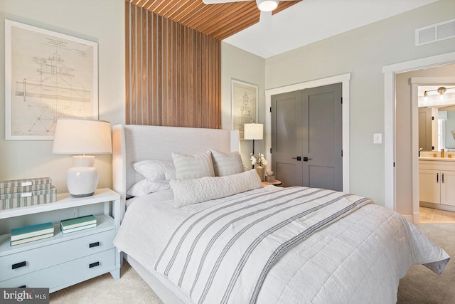 bedroom featuring a ceiling fan, visible vents, a closet, connected bathroom, and light carpet