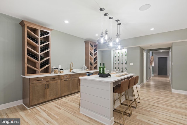 bar featuring indoor wet bar, pendant lighting, baseboards, and light wood-type flooring