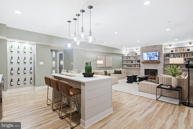kitchen with light wood-style floors, hanging light fixtures, a kitchen island, and a stone fireplace