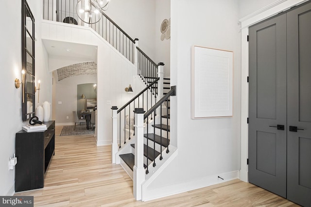 entryway featuring arched walkways, baseboards, light wood finished floors, a high ceiling, and stairs