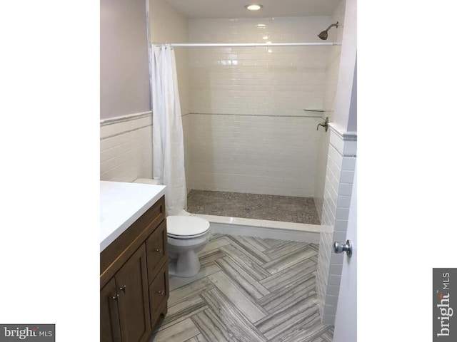 bathroom with a shower with curtain, vanity, tile walls, and toilet