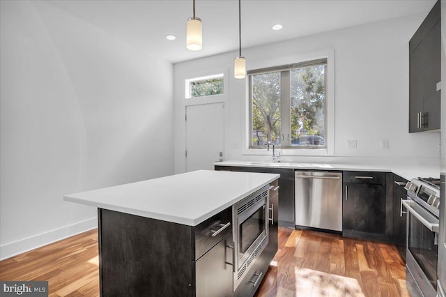 kitchen with stainless steel appliances, pendant lighting, light wood-type flooring, and a center island