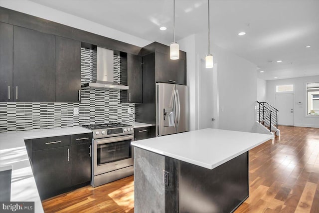 kitchen featuring wall chimney exhaust hood, a kitchen island, light hardwood / wood-style flooring, stainless steel appliances, and hanging light fixtures