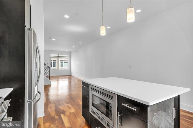 kitchen featuring stainless steel appliances, decorative light fixtures, a kitchen island, and light hardwood / wood-style flooring