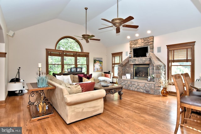 living area with high vaulted ceiling, ceiling fan, wood finished floors, and a stone fireplace