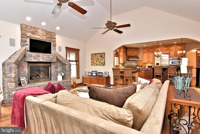 living room with ceiling fan with notable chandelier, a stone fireplace, light hardwood / wood-style flooring, and high vaulted ceiling