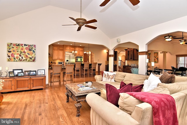 living room with ceiling fan with notable chandelier, high vaulted ceiling, and light hardwood / wood-style flooring