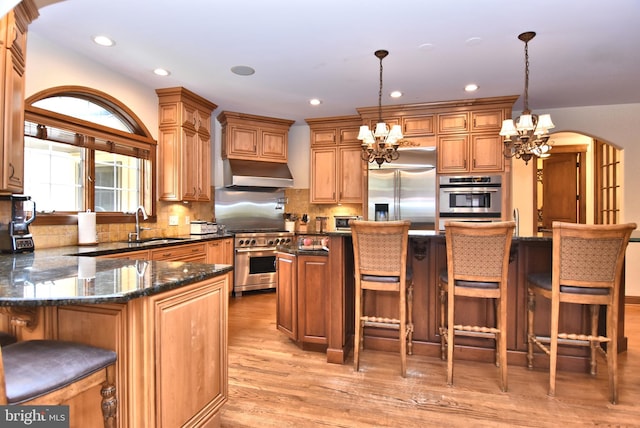 kitchen featuring high quality appliances, a sink, a chandelier, under cabinet range hood, and arched walkways