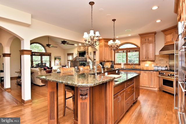 kitchen with a breakfast bar, light wood-type flooring, high end stainless steel range oven, pendant lighting, and ceiling fan with notable chandelier