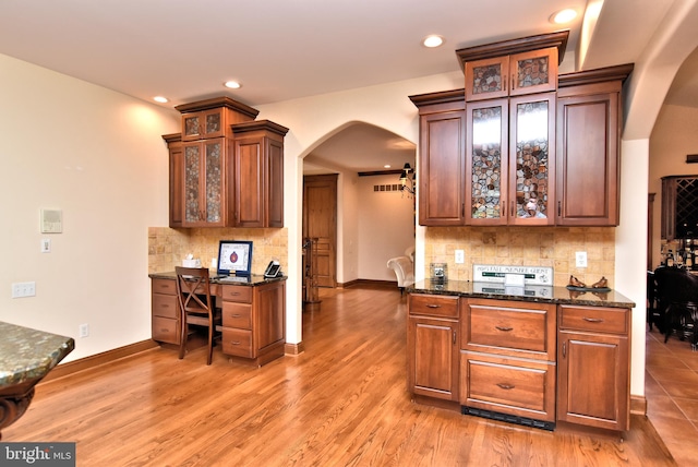 kitchen with dark stone counters, decorative backsplash, built in desk, and hardwood / wood-style flooring