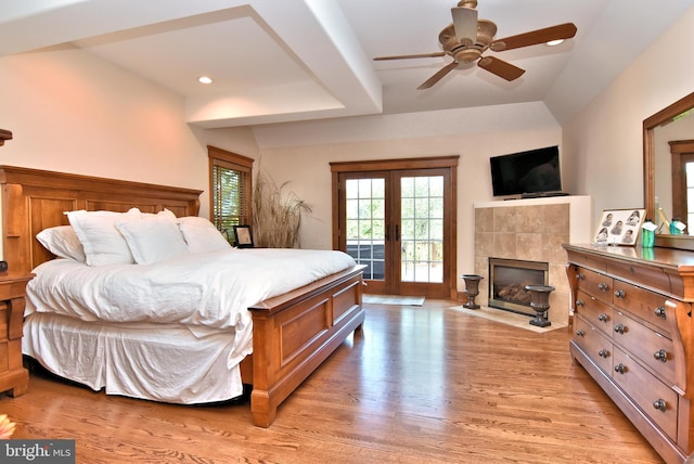 bedroom featuring light wood-type flooring, access to exterior, a fireplace, ceiling fan, and french doors