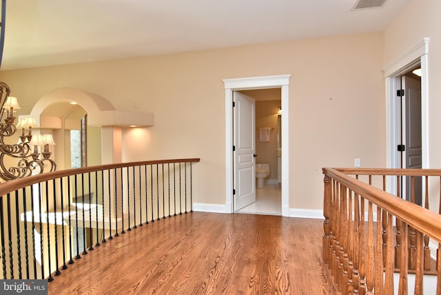 hallway featuring baseboards, an upstairs landing, wood finished floors, and a chandelier