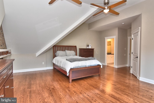 bedroom featuring connected bathroom, a ceiling fan, wood finished floors, lofted ceiling, and baseboards