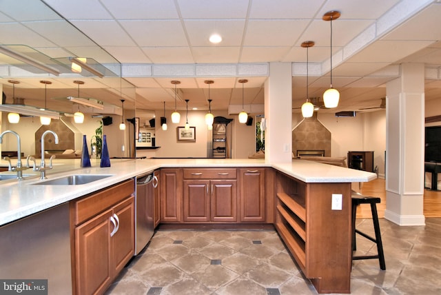 kitchen with pendant lighting, sink, kitchen peninsula, stainless steel dishwasher, and a kitchen bar