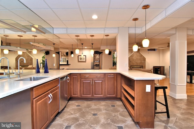 kitchen featuring light countertops, a sink, a kitchen bar, brown cabinets, and open floor plan