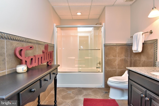 bathroom with tile walls, bath / shower combo with glass door, tile patterned floors, vanity, and a drop ceiling
