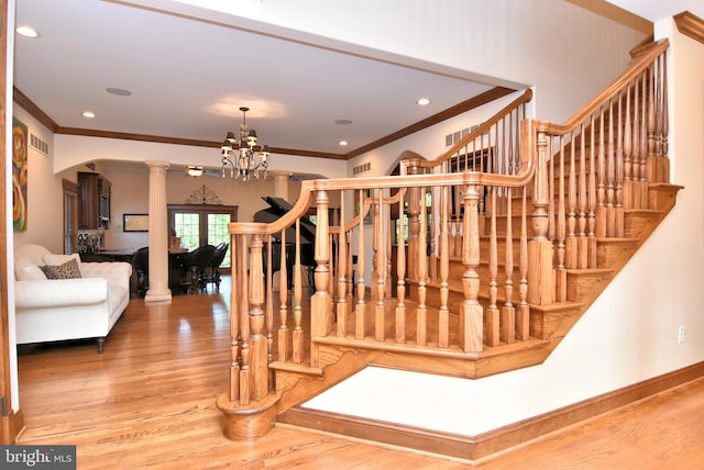 stairs featuring an inviting chandelier, decorative columns, ornamental molding, and hardwood / wood-style floors