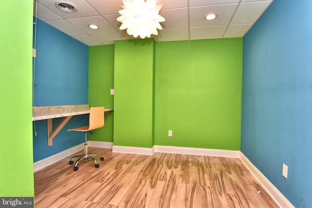 unfurnished office featuring a paneled ceiling, wood finished floors, baseboards, and visible vents